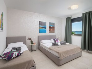 A hotel room with two beds, a small table with a vase, and artwork on the wall.