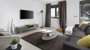Un salon moderne avec un téléviseur à écran plat, un canapé gris et une table basse.