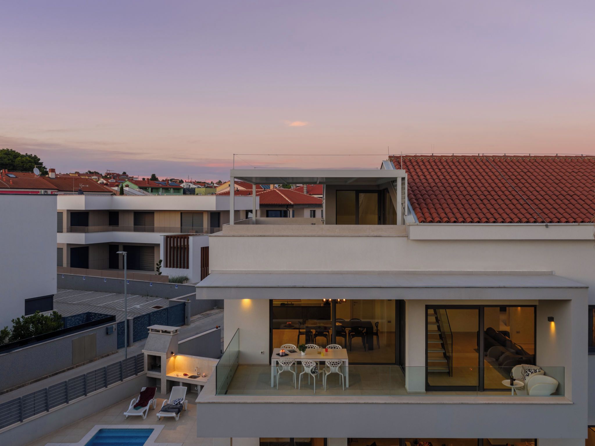 A modern residential building with a rooftop pool, a dining area, and a view of the neighborhood.