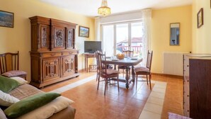 Een woonkamer met een eettafel, stoelen, een bank, een televisie en een grote houten kast.