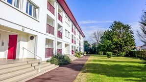 Een meerlaags gebouw met balkons, een rode deur en een pad dat naar de ingang leidt.