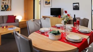 A dining area with a round table set for four, a sofa, a TV, and artwork on the walls. - Allod Park Haus C 603 by Interhome (Davos)