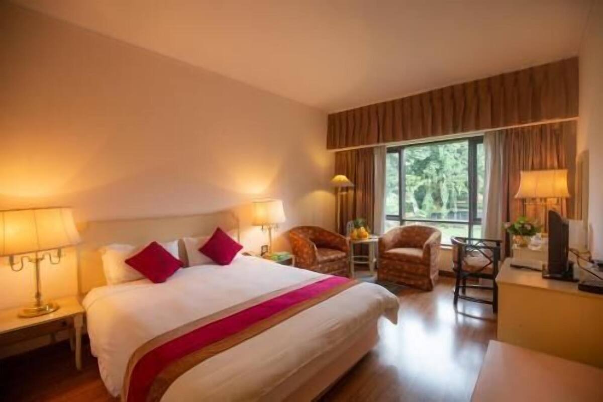 A hotel room with a large bed, two chairs, a desk, and a window.