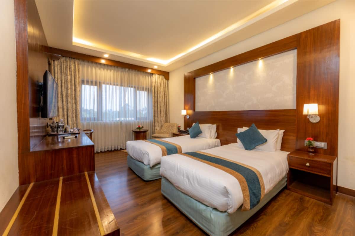 A hotel room with two beds, a desk, and a large window with curtains.