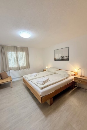 A bedroom with a bed, bedside table, lamp, and a picture on the wall.
