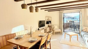 A modern dining area with a wooden table set for four, a television, and a view of a balcony with outdoor seating. - Residenza Chesa Margun 58-5 by Interhome (Silvaplana-Surlej)
