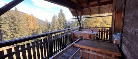 A wooden deck with a bench and a table, overlooking a forested area.