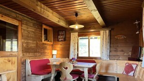 A cozy cabin interior with wooden walls, a dining table with chairs, and a bench area. - Wassertheureralm by Interhome (Dellach)