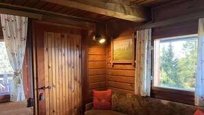 A wooden cabin interior with a sofa, a door, and a window with a painting. - Wassertheureralm by Interhome (Dellach)