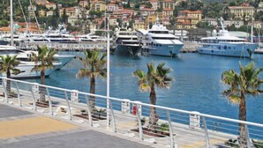 A marina with yachts docked, palm trees, and a hillside of colorful buildings in the background. - Borgoverde by Interhome (Imperia)