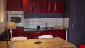 Eine kompakte Küche mit roten Schränken, einem eingebauten Backofen, einer Spüle und einem Esstisch mit Stühlen.