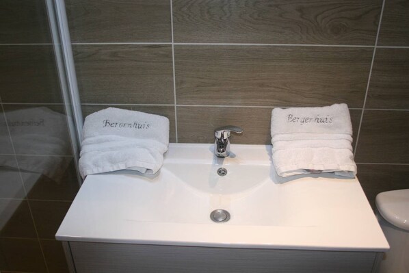 Ein Badezimmer mit einem weißen Waschbecken, zwei mit „Berengar's“ beschrifteten Handtüchern und einem Spiegel über dem Waschbecken.