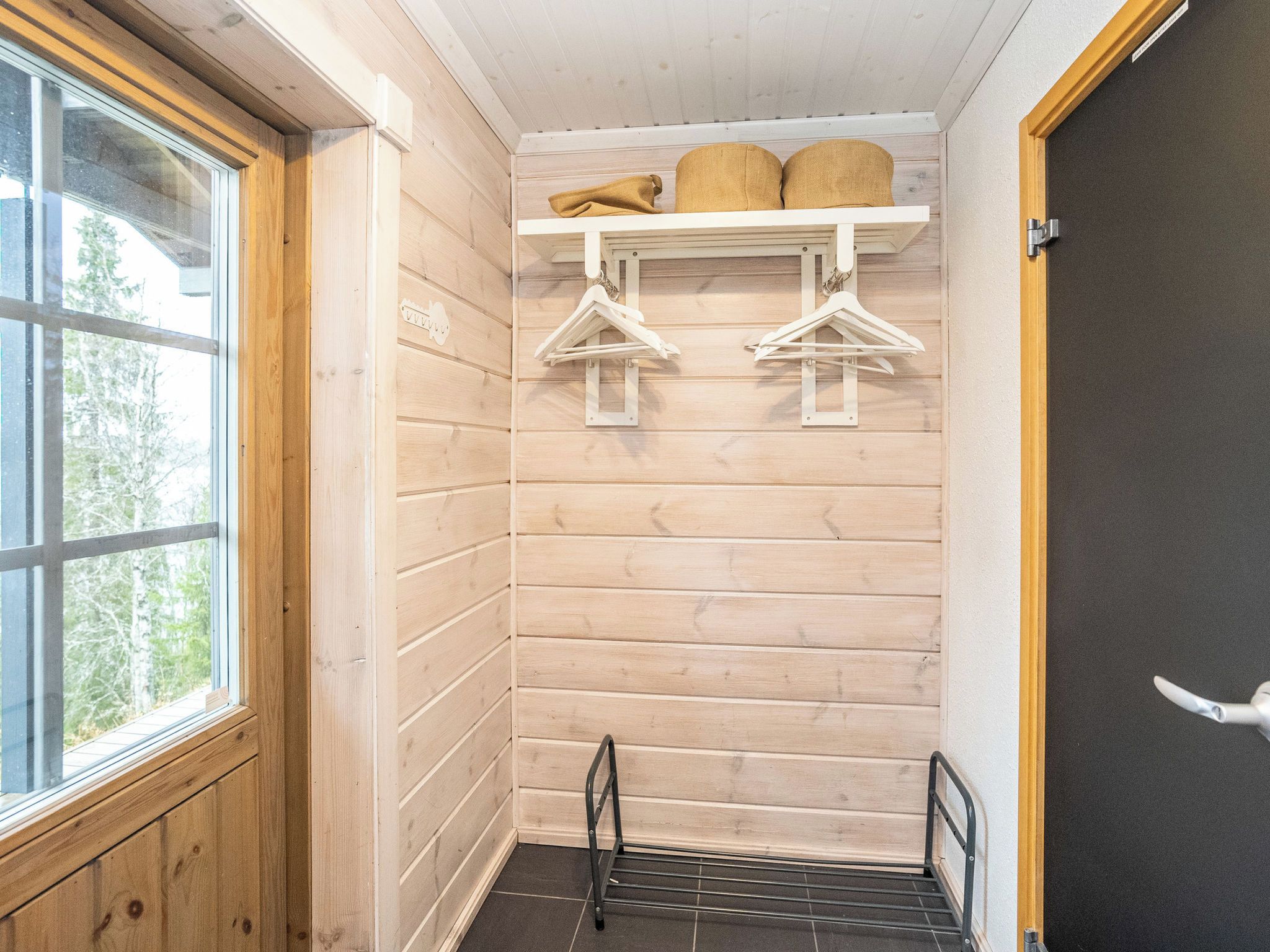 A corner room with wooden walls, a window, a door, and a metal rack with hangers.