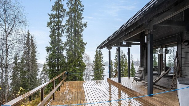 En træterrasse med gelænder, der kigger ud over en skov og et vandområde.