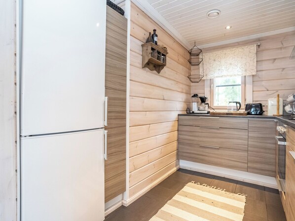 Una cocina con armarios de madera, un refrigerador empotrado y un ventanal con cortina floral.