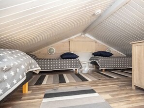 A room with two beds, a wooden ceiling, and a striped rug.
