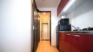 A narrow hallway with wooden flooring leading to a door. There are shoes lined up against the wall, a microwave, and a sink on the right side. - Grandouce Juso (Osaka)