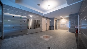 A modern elevator area with a row of elevators, a fire extinguisher, and a wall-mounted sign. - Grandouce Juso (Osaka)