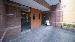 A modern building entrance with a glass door, a brown wooden panel, and a signboard. - Grandouce Juso (Osaka)