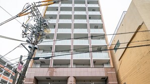A multi-story building with a prominent entrance, a parking lot with marked lanes, and a visible utility pole with wires. - Grandouce Juso (Osaka)