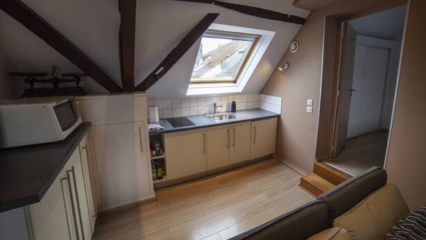 Cocina compacta con tragaluz, vigas de madera y encimera moderna.