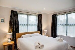 A hotel room with a bed, two bedside lamps, a window with curtains, and a framed picture on the wall.