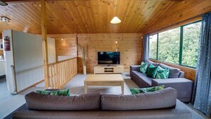Ein gemütliches Blockhausschlafzimmer mit Holzbalkendecke, einem Fernseher, einer Couch und einem Fenster mit Blick auf Grünflächen.