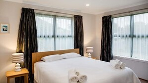 Ein Hotelzimmer mit einem großen Bett, zwei Nachttischlampen, einem gerahmten Bild an der Wand und einem Fenster mit Vorhängen.