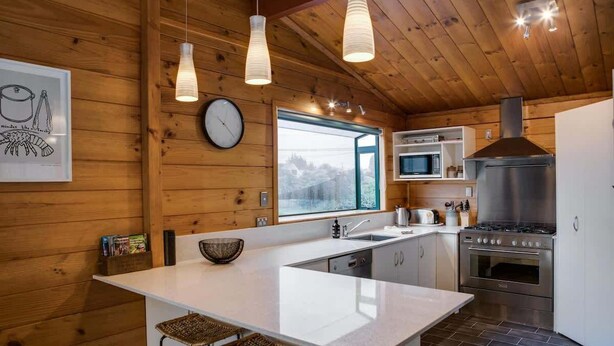 Eine moderne Küche mit Holzwänden, einer großen Kochinsel, Edelstahlgeräten und Blick durch das Fenster.