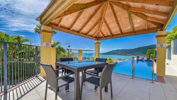 A covered outdoor area with a pool, a dining table with chairs, and a view of the sea. - Ocean Views Galore - Airlie Beach (Cannonvale)