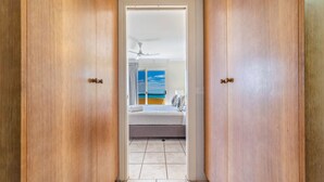 A hallway leading to a bedroom with a bed, a ceiling fan, and a view of the sea through a window. - Ocean Views Galore - Airlie Beach (Cannonvale)