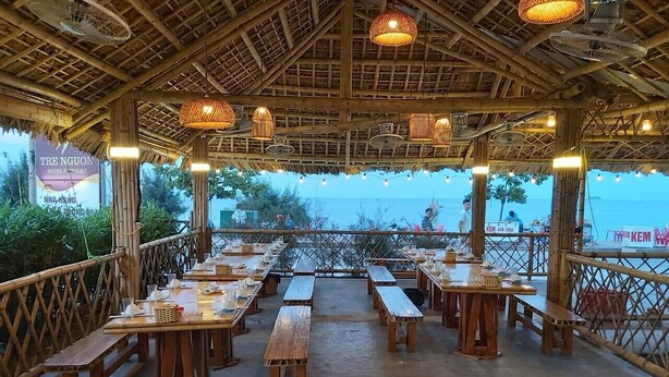 An outdoor dining area with wooden tables and benches, bamboo ceiling, and hanging lights.