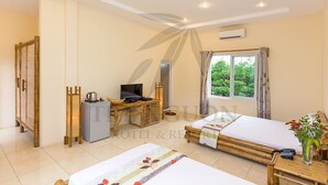 A hotel room with a bed, a desk with a TV, a small fridge, and a window with a view of greenery.