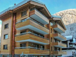 Un immeuble en bois à plusieurs étages, doté de balcons, qui se dresse sur un fond de paysage montagneux.