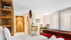 Una camera d'albergo con un letto grande, un armadio in legno, un'area pranzo e una finestra con tende leggere.