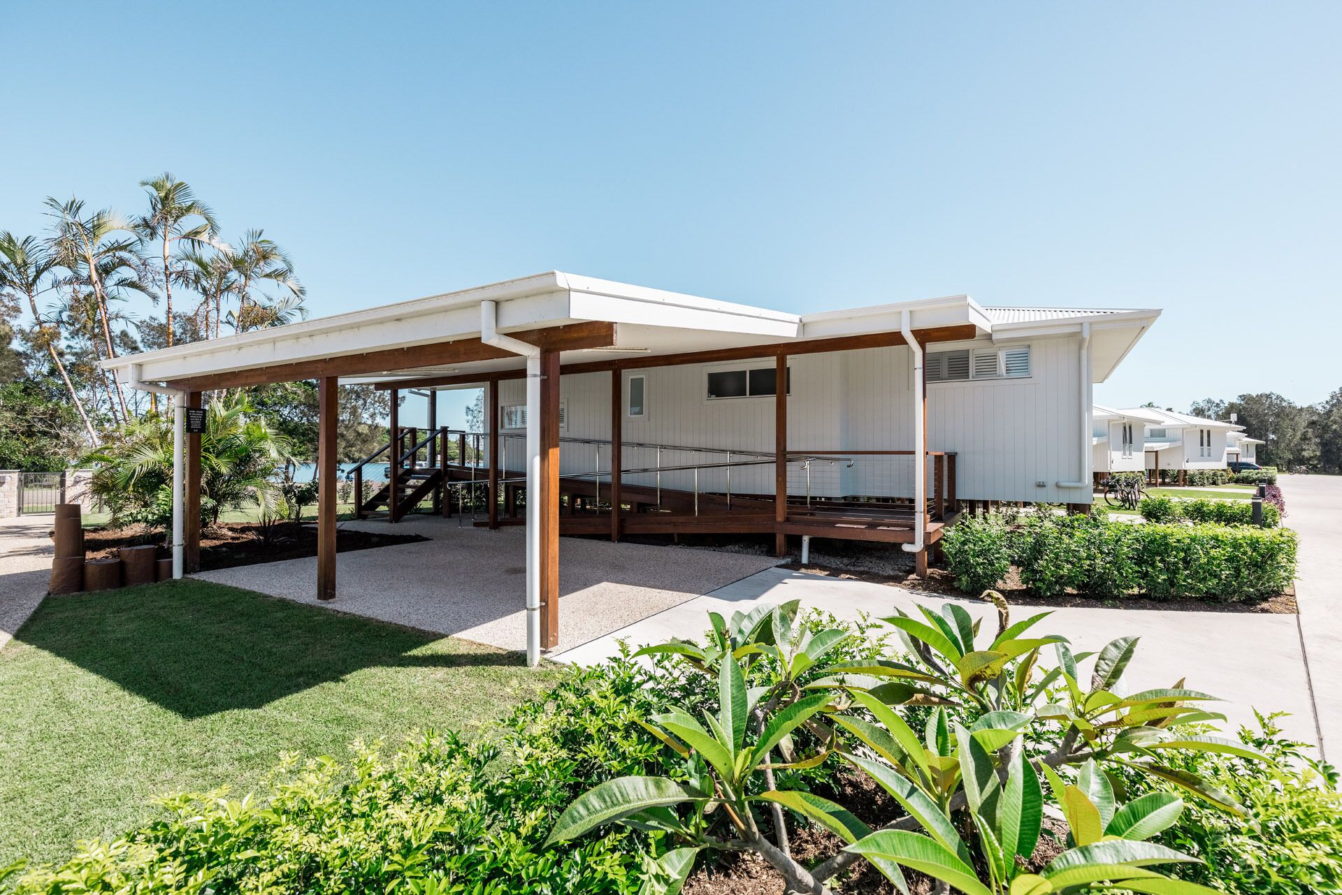 Un bâtiment moderne, de plain-pied, doté d’un patio couvert, entouré d’une végétation luxuriante et de palmiers.