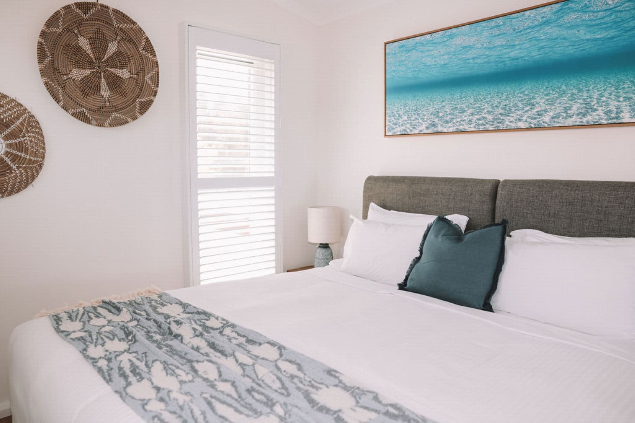 A bedroom with a bed, a nightstand, a lamp, and a wall with two woven wall hangings.