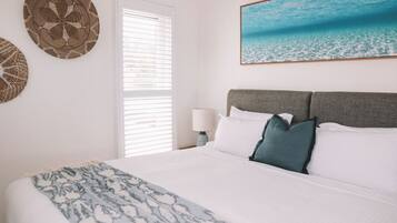 A bedroom with a bed, a nightstand, a lamp, and a wall with two woven wall hangings.