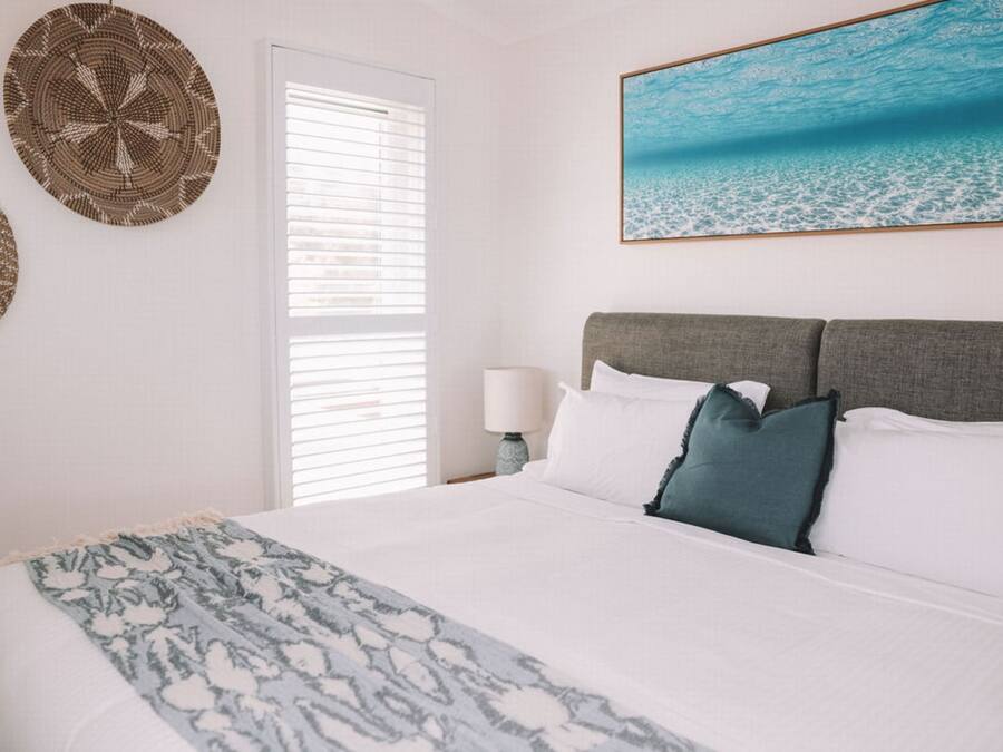 A bedroom with a bed, a nightstand, a lamp, and a wall with two woven wall hangings.