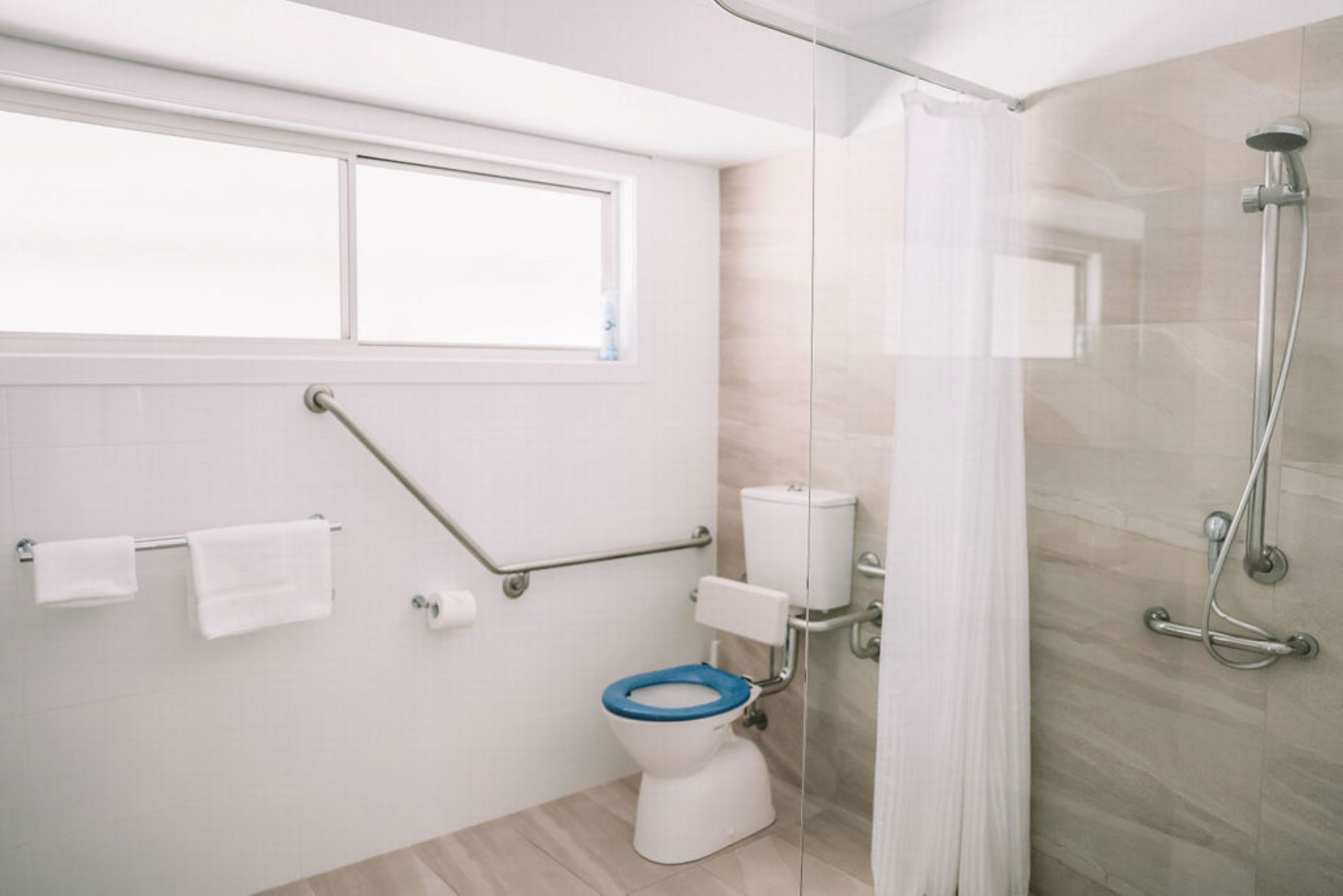 A modern bathroom with a toilet, grab bars, a shower, and a window.