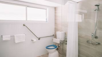 A modern bathroom with a toilet, grab bars, a shower, and a window.