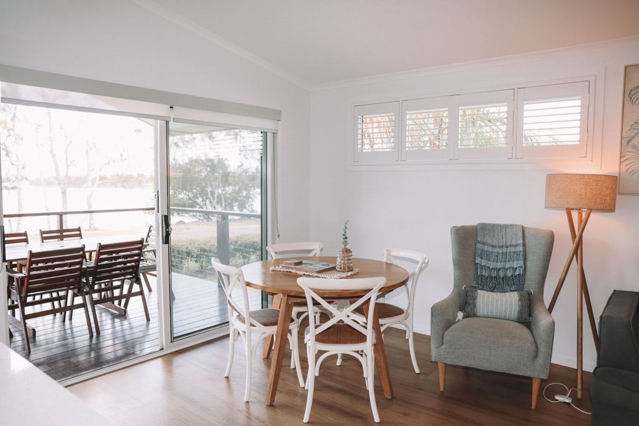 A dining area with a round table and white chairs, a grey armchair, and a floor lamp.