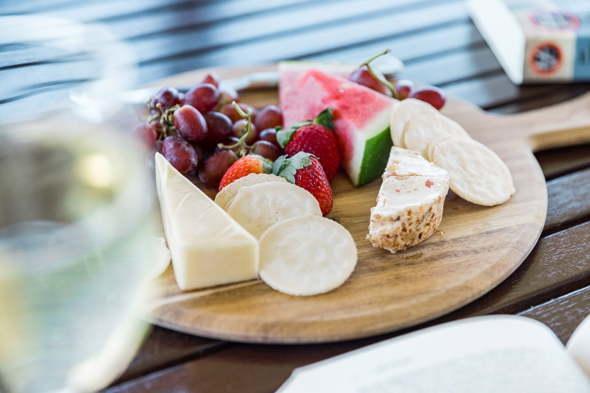 A wooden board with cheese, grapes, strawberries, and a slice of watermelon.