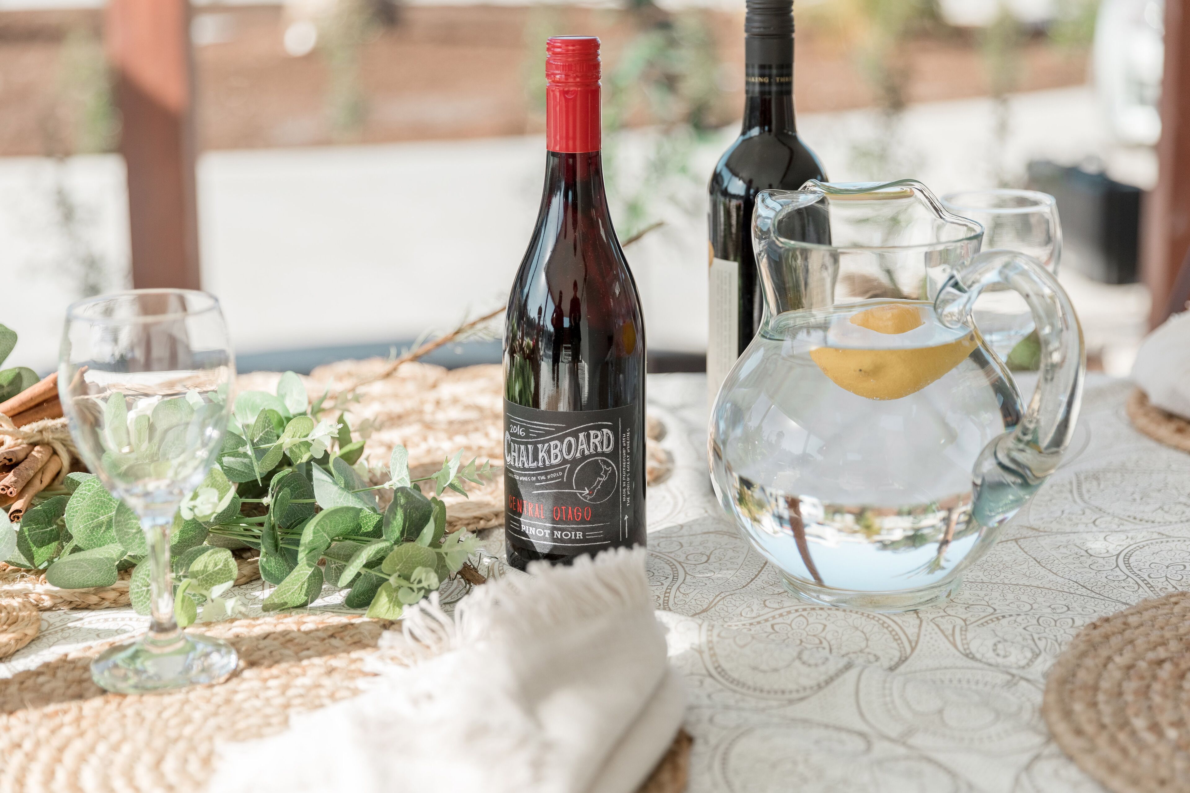 A table with a wine bottle, glasses, and a pitcher of water.