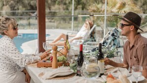 A dining table set with wine bottles, glasses, and a fruit platter, overlooking a pool area.