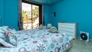 A bedroom with a bed, a ceiling fan, a window with curtains, a white dresser, and a fan on the floor. - Parque Santiago II 228 - Two Bed (Playa de la Américas)