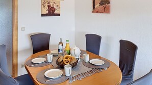 A round dining table with four chairs, a bottle of orange juice, a bottle of water, a basket of pretzels, and a teapot.