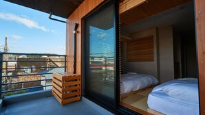 A modern bedroom with a large sliding glass door, a wooden bench, and a view of the cityscape. - KAMAKURA Hotel (Kamakura)