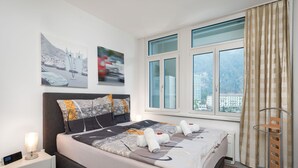 Ein modernes Hotelzimmer mit einem großen Bett, einem Nachttisch, einer Lampe und einem Fenster mit Vorhängen.