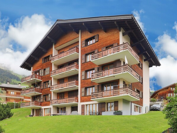 A multi-story hotel with balconies, a flat roof, and a mountainous backdrop. - Beausoleil 14 by Interhome (Verbier)